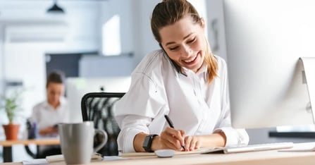 Corporate travel planner on phone, writing notes down for an upcoming trip
